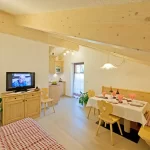 Soggiorno accogliente con tavolo da pranzo imbandito e TV accesa vicino a una cucina a vista