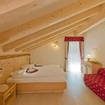 Camera da letto mansardata in legno con letto matrimoniale e divano rosso a fantasia