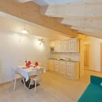 Accogliente soggiorno con cucina open space in legno, divano verde e angolo pranzo