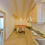 Cucina e sala da pranzo in legno, moderna e accogliente, con tavolo apparecchiato e vista verso una camera da letto